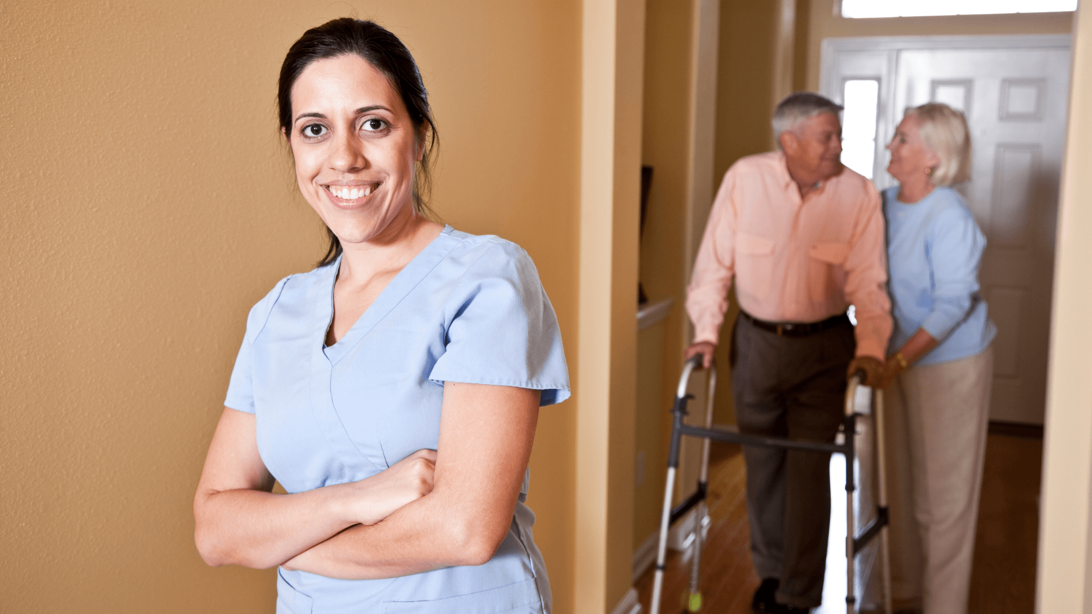 Female caregiver wearing uniform crossing arms with old couple at the back