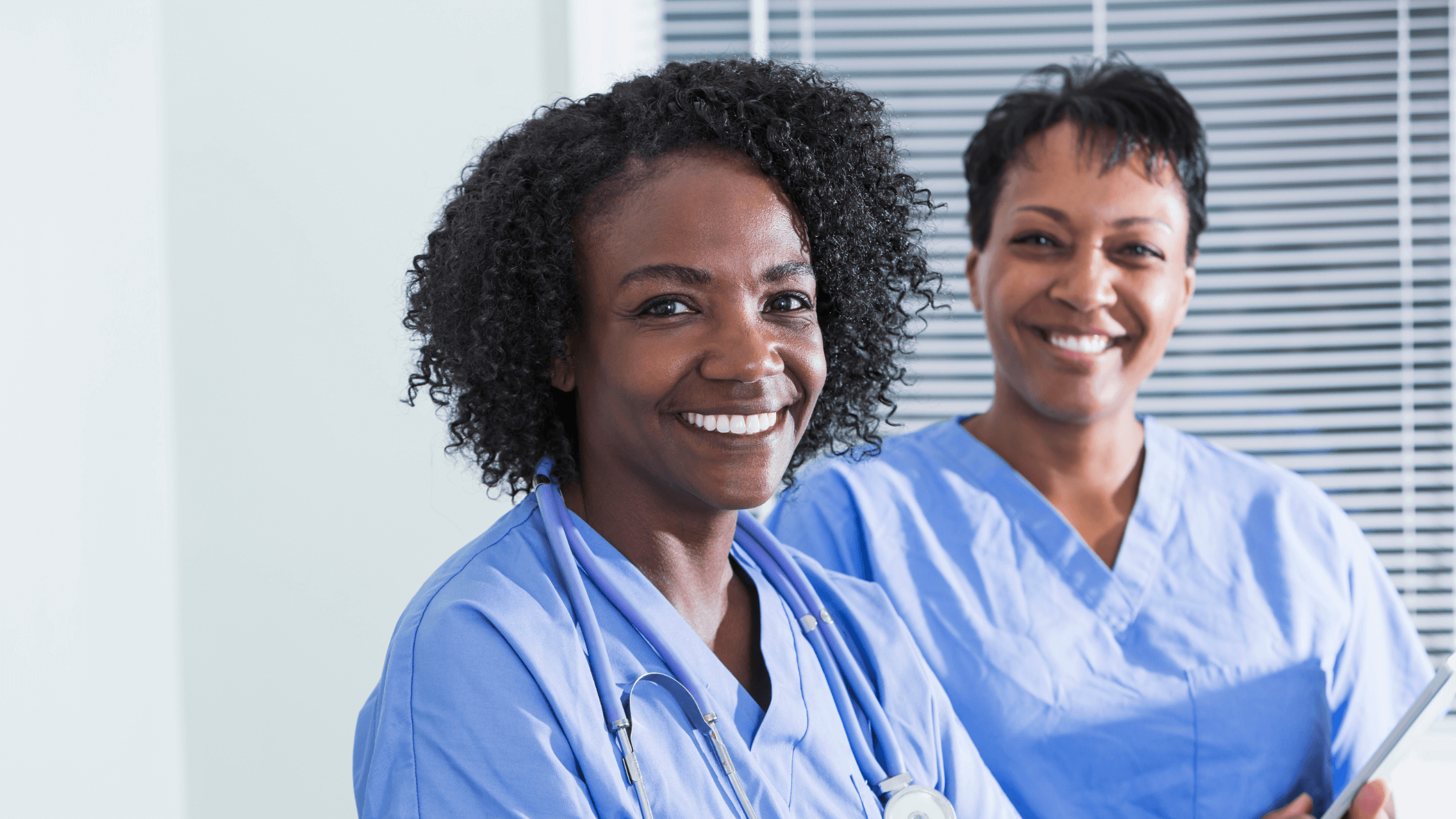 Two woman of color caregiver with natural hair wearing uniform smiling