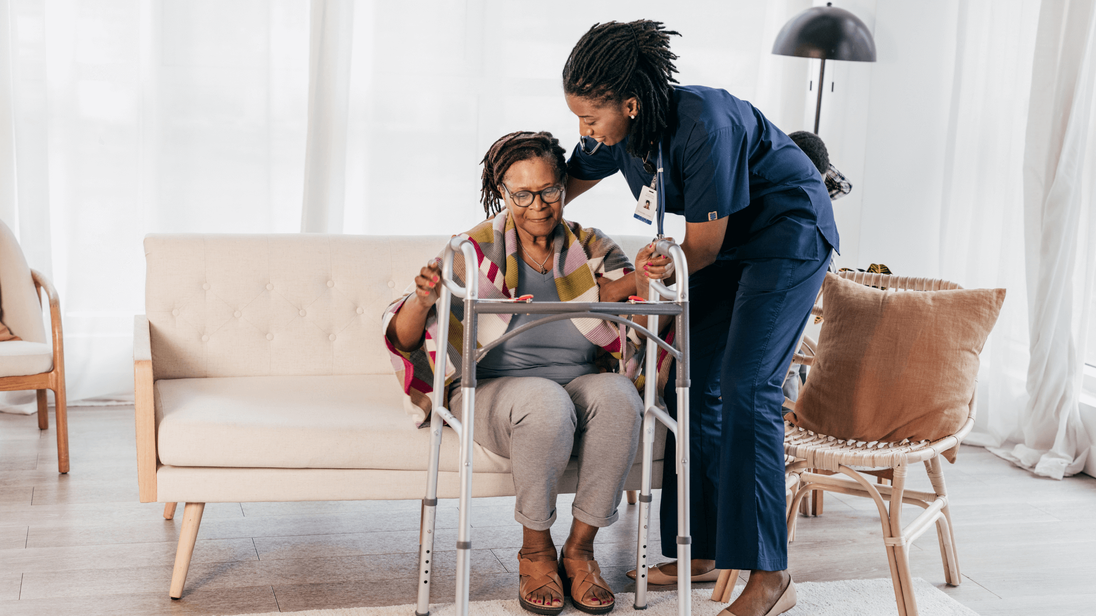 Female caregiver assisting senior woman to standing using her standing aid in home